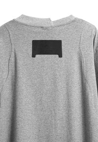 Sudadera gris con cuello alto, tejido texturizado y una etiqueta rectangular negra en la parte posterior con texto en relieve.