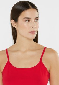 Red tank top made of smooth fabric, featuring thin straps and a fitted design, displaying a clean neckline and minimal stitching details.