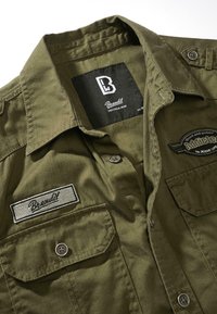 Kortermet skjorte i olivengrønn laget av bomull. Har to frontlommer, logo-patcher og knappestengning. Klassisk krage.