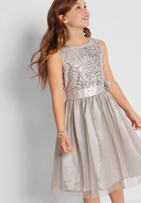 Robe en sequins argentés avec un design sans manches, une ceinture en satin et un accent floral ; la jupe en tulle plissé ajoute du volume et de la structure.