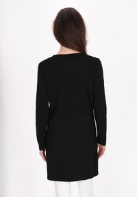 T-shirt tunica nera a maniche lunghe con una vestibilità rilassata, scollatura rotonda e tessuto morbido, che arriva sotto i fianchi, abbinata a pantaloni bianchi.