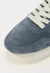 Baskets en cuir bleu avec une pointe arrondie, lacets blancs et semelle en caoutchouc de couleur claire. La tige présente des détails de couture pour la structure.