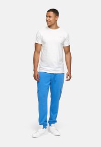 Weißes Kurzarm-T-Shirt mit Rundhalsausschnitt, kombiniert mit leuchtend blauen Jogginghosen mit Seitentaschen und weißen Sneakers.
