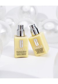 Dwie żółte butelki kosmetyków do pielęgnacji skóry Clinique z srebrnymi pompkami. Jedna to nawilżające mleczko, druga to żel. Etykiety są widoczne.