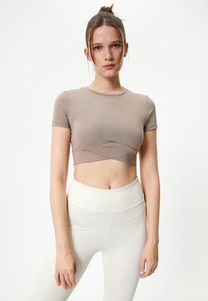 Afkortet, kortærmet t-shirt i lysebrun stof med et twist-design ved taljen, parret med højalmede, cremede leggings.