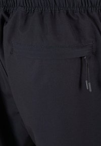 Sorte elastiske bukser med strikk i livet, baklomme, snøring og glatt, matt tekstur. Enkel design uten synlige mønstre.
