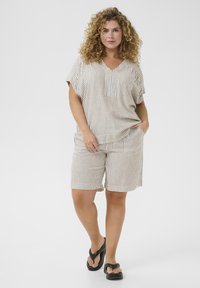 Conjunto de mezcla de lino que incluye una blusa de cuello en V y manga corta con bolsillo y pantalones cortos a rayas. Los colores incluyen crema y tonos tierra, con tejido texturizado.