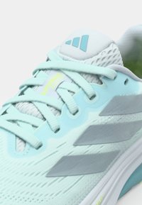 Scarpa da ginnastica azzurro chiaro con accenti grigi, tomaia in rete, lacci piatti e un logo sulla linguetta. Presenta un motivo testurizzato e una suola imbottita.