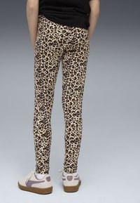 Leggings stampati leopardati in beige e marrone, con una vestibilità slim. Abbinati a sneakers crema con dettagli viola e suole marroni.