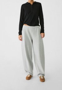 Czarna longsleeve polo z zapięciem na guziki, w połączeniu z jasnoszarymi, luźnymi spodniami dresowymi z miękkiego materiału. Brązowe buty sportowe.