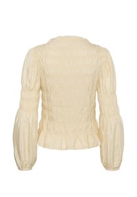 Blouse couleur crème avec de longues manches bouffantes, détails élastiqués froncés sur le corps et les manches, et un petit volant à l'ourlet et au col.