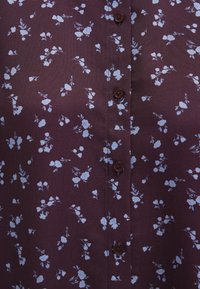 Dark purple shirt featuring a floral pattern in light blue. Brown buttons at the front enhance its design. Soft, lightweight fabric.