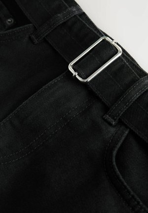 Mustad teksapüksid tekstuurse pinnaga, millel on hõbedane metallist pandlaga vöö, vööaasad ja kontrastsed õmblused õmbluste ääres.