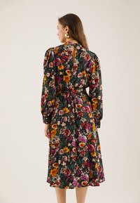 Blommig klänning med långa ärmar, svart bakgrund, livfulla färger inklusive röda, gula och lila blommor, cinchad midja, nyckelhålsdetalj bak.
