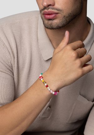 Farverig perlearmbånd med røde, hvide, rosa, gule og turkise perler, der har glatte og matte teksturer, båret på en hånd.