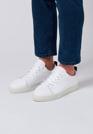 Baskets en cuir blanc avec un design bas, bout rond et semelle en caoutchouc texturé, agrémentées d'accents minimalistes et de lacets plats.