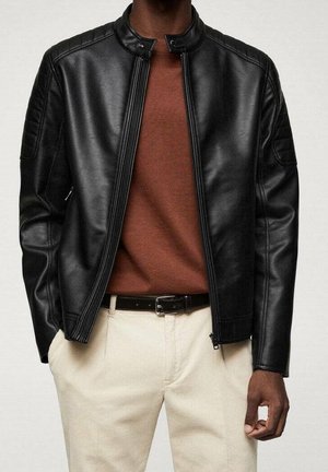 Black leather jacket with a round collar, zip front, and textured shoulder detailing, worn over a brown shirt and cream pants.