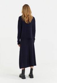 Ensemble en maille marine comprenant un pull et une jupe à coupe décontractée ; présente des poignets côtelés et une jupe droite. Assorti à des bottines noires.