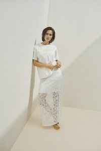 T-shirt blanc en coton avec inscription "Solar" en jaune, associé à une longue jupe en dentelle blanche. Le modèle porte des tongs jaunes.