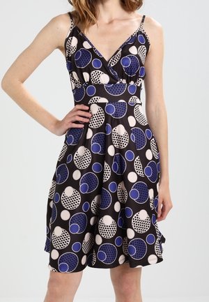 Robe noire avec un décolleté en V, des bretelles réglables et une jupe évasée. Le tissu présente de grands cercles en pois bleus, blancs et noirs.