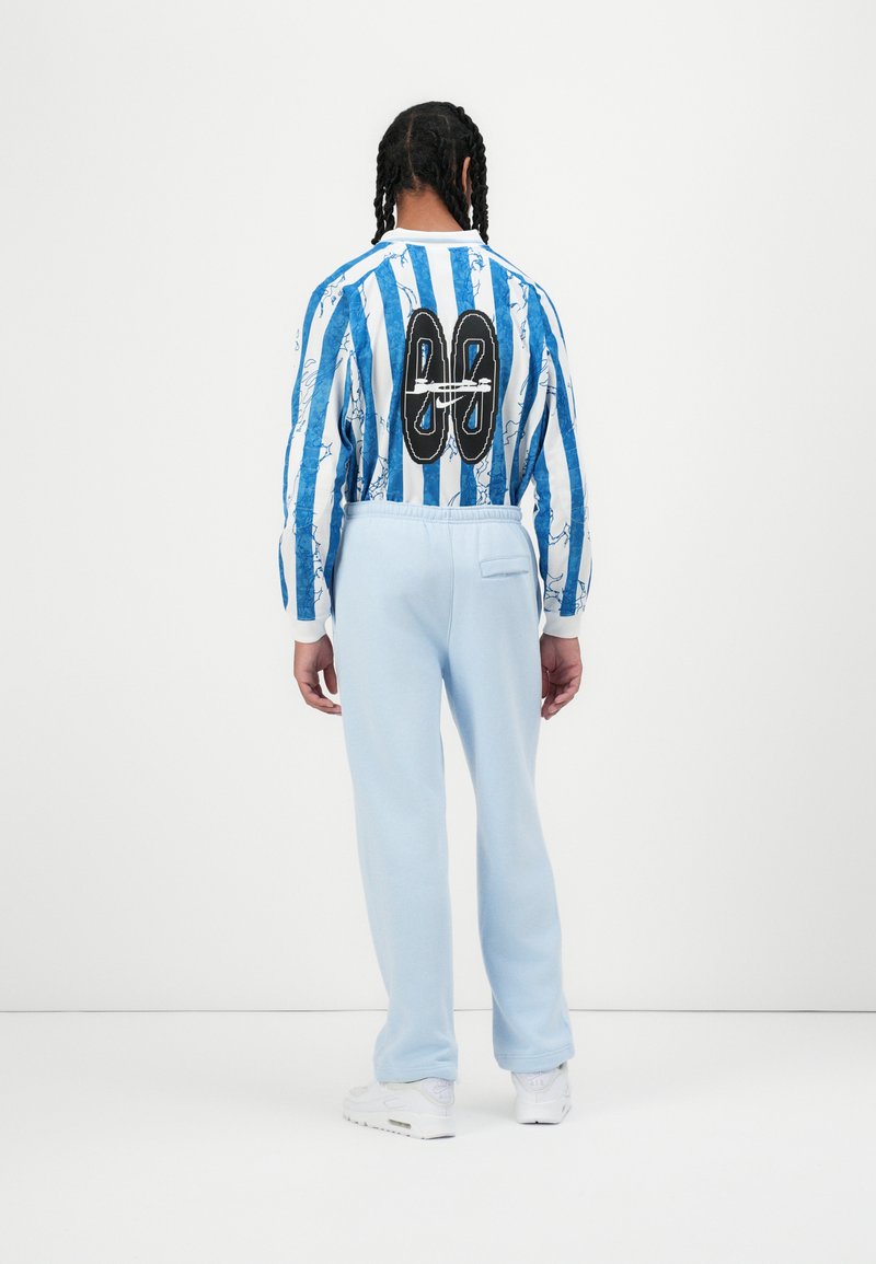 Gestreiftes blau-weißes Langarmhemd mit einem grafischen Design auf dem Rücken, kombiniert mit hellblauen Sweatpants aus weichem Stoff.