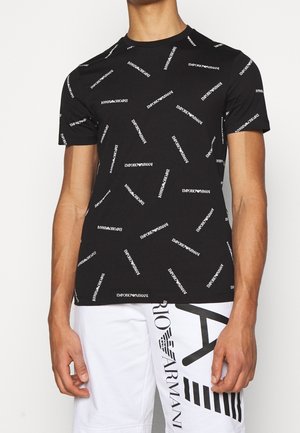 Chemise noire à manches courtes avec le texte blanc répété "Emporio Armani", associée à un short blanc affichant un grand logo Armani noir et du texte.