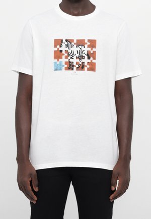 T-shirt blanc avec un motif de zèbre réalisé en pièces de puzzle, avec une pièce bleue manquante sur un fond marron.
