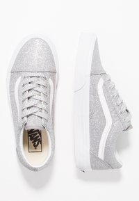 Baskets pailletées argent avec des accents blancs, des lacets plats et un design classique à tige basse. La semelle en caoutchouc est blanche et texturée pour une meilleure adhérence.