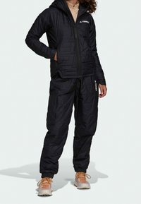 Sort isoleret jakke med lynlås foran og hætte, kombineret med matchende bukser. Begge har et struktureret mønster og elastiske manchetter.