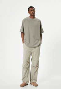 Løs pasform, taupe bomulds T-shirt med korte ærmer; beige, letvægtsbukser med lommer; brune slip-on sko; neutral baggrund.