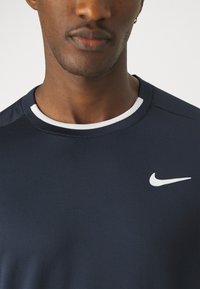 Marineblå Nike treningsskjorte med hvit kragekant og logo. Glatt, strukturert stoff med korte ermer, egnet for sport eller hverdagsbruk.