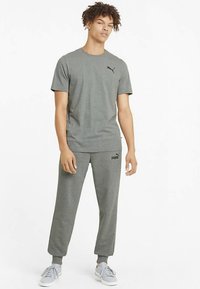 Graues Baumwoll-T-Shirt mit kurzen Ärmeln und einem schwarzen Logo auf der linken Brust, kombiniert mit grauen Joggerhosen mit elastischem Bund und Bündchen.