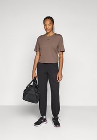 Brun kortärmad t-shirt, svarta träningsbyxor, svarta sneakers med rosa detaljer, håller en svart gymväska. En enkel och funktionell aktiv klädsel.