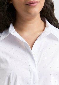 Witte blouse met kraag, voorzien van een subtiel patroon van kleine edelsteenvormige accenten gelijkmatig verdeeld over de stof. Knopsluiting.