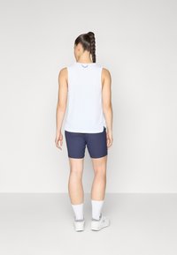 White sleeveless top with a round neckline, paired with navy shorts. White sport socks and light gray athletic shoes with accented details.