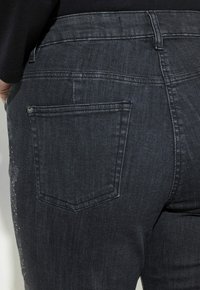 Jeans de mezclilla oscura con corte recto, con un pequeño bolsillo trasero y un sutil desgaste. Tejido texturizado con detalles de costura tonales.