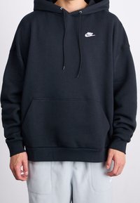 Black cotton hoodie with a drawstring hood, kangaroo pocket, and white Nike logo on the chest. Features ribbed cuffs and hem.