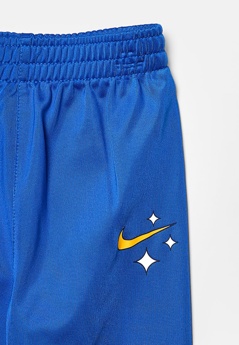 Pantaloni shorts blu realizzati in un tessuto liscio e elastico con una vita elasticizzata. Presentano un logo Nike giallo e tre accenti a forma di stella in bianco.
