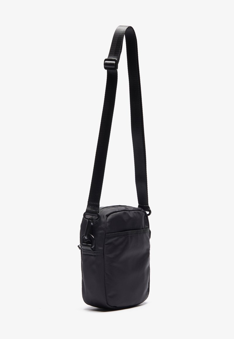 Bolso bandolera negro de nailon con una sola correa ajustable, compartimento principal con cremallera y bolsillo frontal. Forma rectangular compacta con una textura suave.