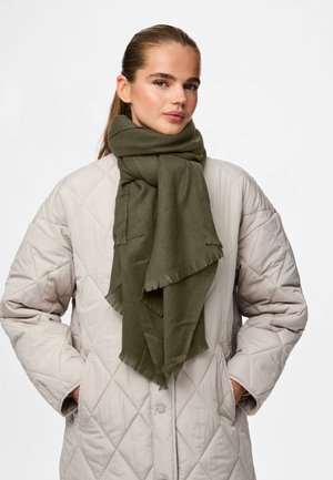 En olivengrøn tørklæde lavet af blødt stof, med frynser i kanten, båret over en lys beige quilted jakke med diamantmønster.