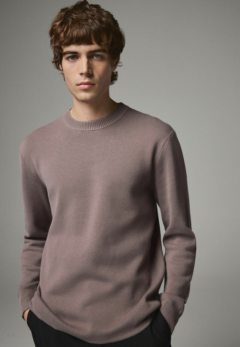 Gestrickter Pullover in sanftem Lavendel mit einem gerippten Rundhalsausschnitt und langen Ärmeln, der eine glatte Textur und ein minimalistisches Design aufweist.