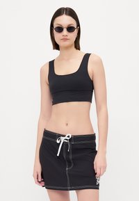 Top corto negro con escote cuadrado combinado con una falda corta negra que cuenta con un cordón y detalles de costura blanca.