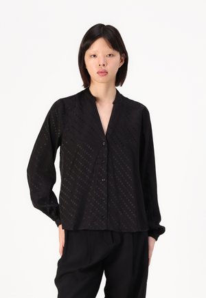 Black blouse featuring a subtle dot pattern, soft fabric, button front, and long sleeves with gathered cuffs. Simple collar design.