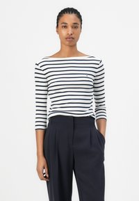 Gestreiftes langärmliges Oberteil in Marineblau und Weiß aus weicher Baumwolle, mit einem Bootsausschnitt und einem kleinen Logo auf der Brust, kombiniert mit maßgeschneiderten schwarzen Hosen.