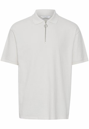 Polo blanco hecho de material suave, con mangas cortas, cuello con cremallera y herrajes plateados, y un diseño de ajuste relajado.