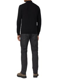 Schwarzer Pullover mit hohem Kragen, figurbetontem Schnitt und gerippten Bündchen, kombiniert mit dunkelblauer Jeans und braunen Wanderschuhen.