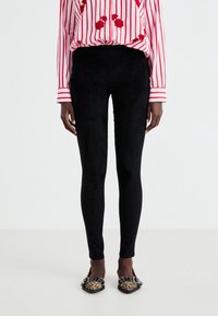 Leggings noirs taille haute en matière douce et extensible avec une texture veloutée, associés à des ballerines imprimé léopard et un chemisier rayé.