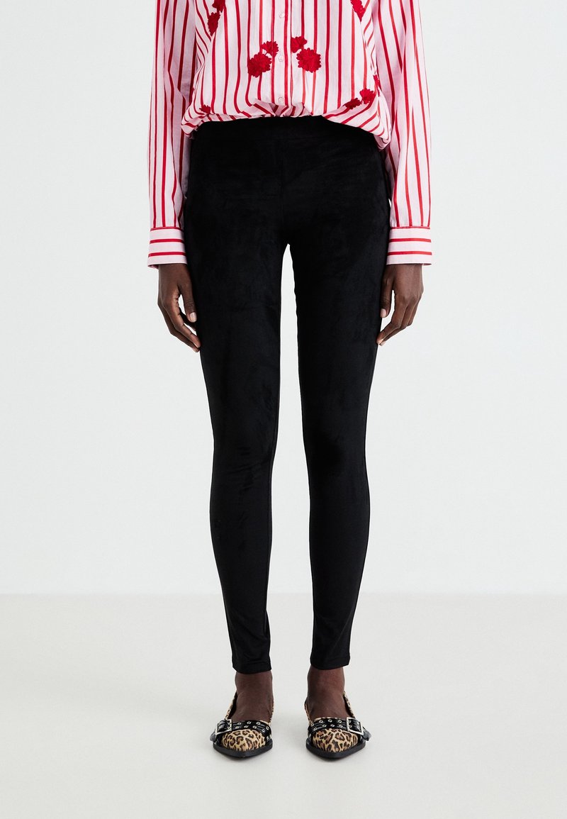 Leggings noirs taille haute en matière douce et extensible avec une texture veloutée, associés à des ballerines imprimé léopard et un chemisier rayé.