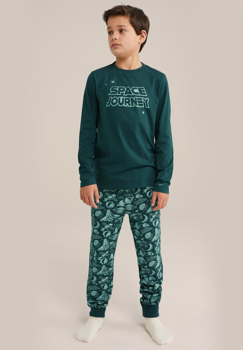 Zeleni dolg rokav pižama zgornji del z odtisom "PRODUŽENA POTOVANJA", v kombinaciji z vzorčastimi zelenimi hlačami, ki imajo vesoljske motive in manšete.