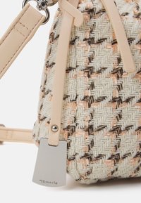 Gros plan d’un sac à main beige tissé avec un motif géométrique, bandoulière en cuir beige et étiquette de marque Tamaris en argent.